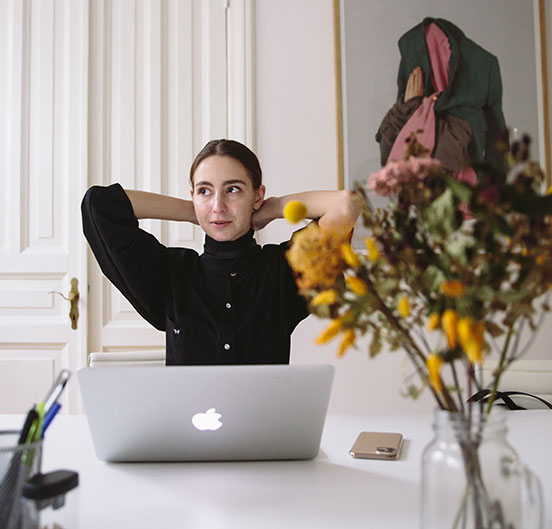 Kvinde sidder foran en computer med armene bag hovedet og ser afslappet ud