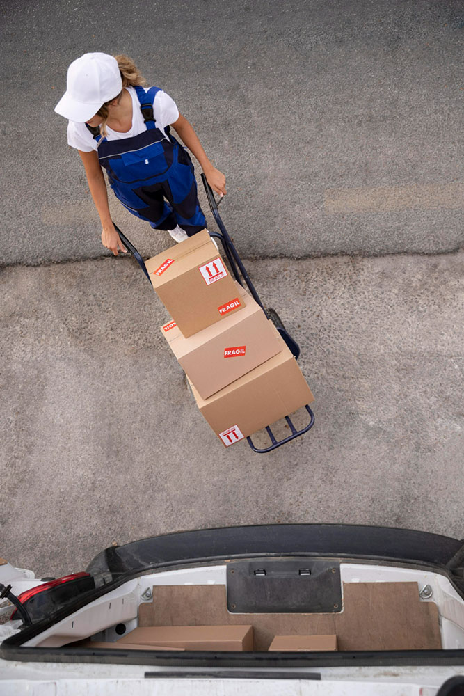 En kvinde i overalls som flytter en stak kasser på en sækkevogn