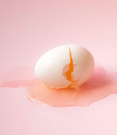 Et knækket æg hvor indholdet løber ud på en lyserød baggrund